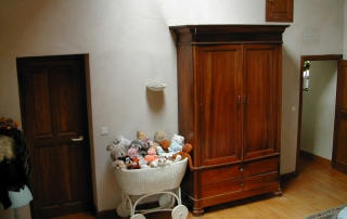 Armoire haute au fond pour ranger vos affaires et berceau décoratif débordant de peluches. A gauche accès à la salle de bans des enfants.