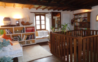 Au rez de chaussée, le salon équipé d'un canapé en cuir blanc en face d'une cheminée ancienne en pierre sur la gauche, avec ses chenêts en fonte.