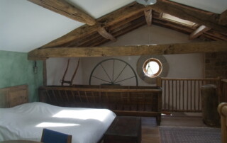 Mezzanine avec meuble mangeoire et ancienne mangeoire en guise de barrière, oeil de boeuf au fond, ancienne meule en décoration, plafond avec poutre en chêne.